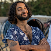 student artist in residence Omar Howaida El-Sabrout smiling with his arms crossed in a floral deep cut blue and white shirt